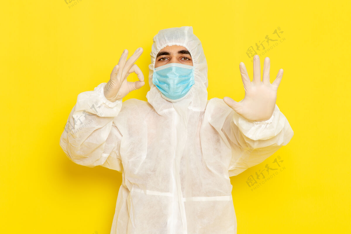科学身穿特殊防护服 戴着面罩的男性科学工作者的正面图 手掌放在淡黄色的墙上人光危险