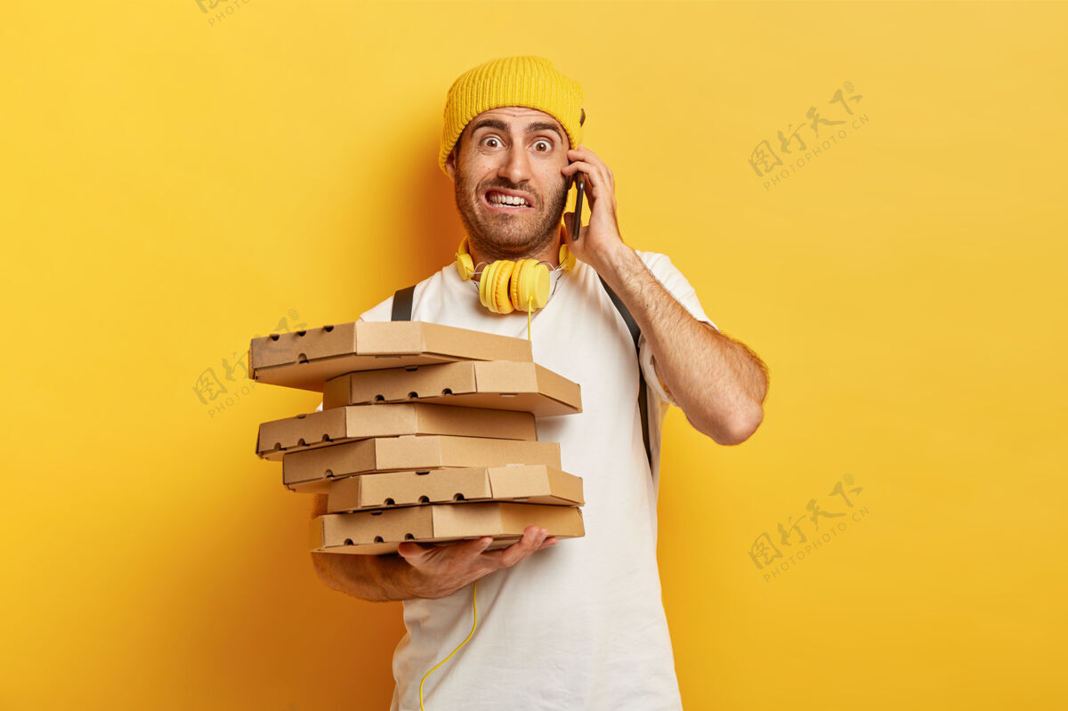 容器照片中的披萨人通过智能手机接受顾客的订单 手里拿着许多装有快餐的纸箱 用不愉快的眼神和不满意的顾客交谈服务和交付理念电话美味堆