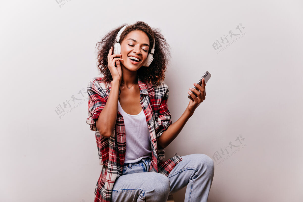 肖像快乐的穿红衫的黑人女孩戴着耳机听音乐快乐的卷发的年轻女子用最喜欢的歌让人心寒音乐活力手机