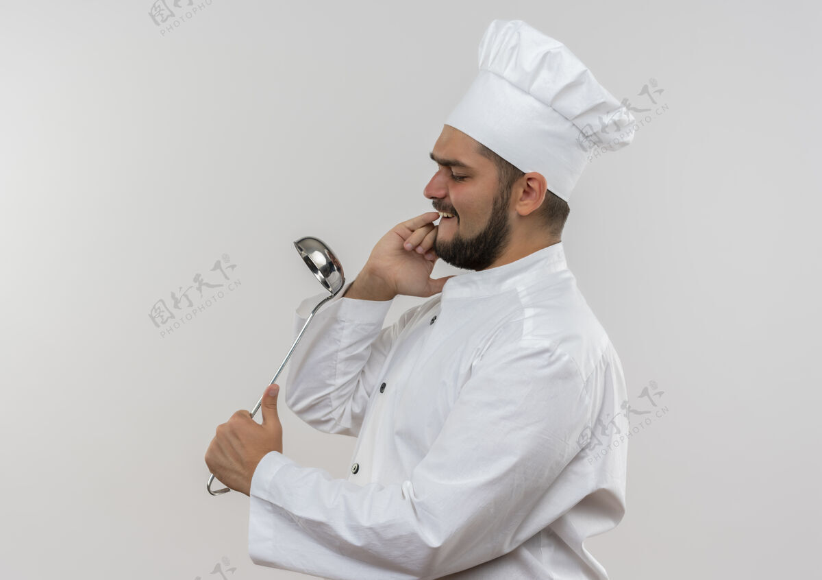 厨师穿着厨师制服的年轻男厨师拿着勺子 把它当作镜子隔离在粉红色的空间里厨师年轻使用