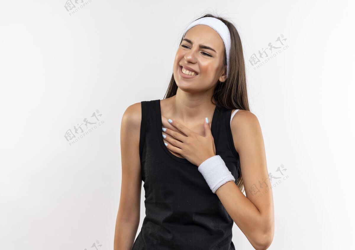复制微笑着漂亮的运动女孩戴着头带和腕带把手放在胸前看着隔离在白色空间的一边戴微笑侧面