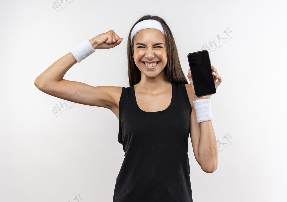 手机微笑着漂亮的运动女孩戴着头带和手环拿着手机做着强烈的手势隔离在空白处手势握持头带