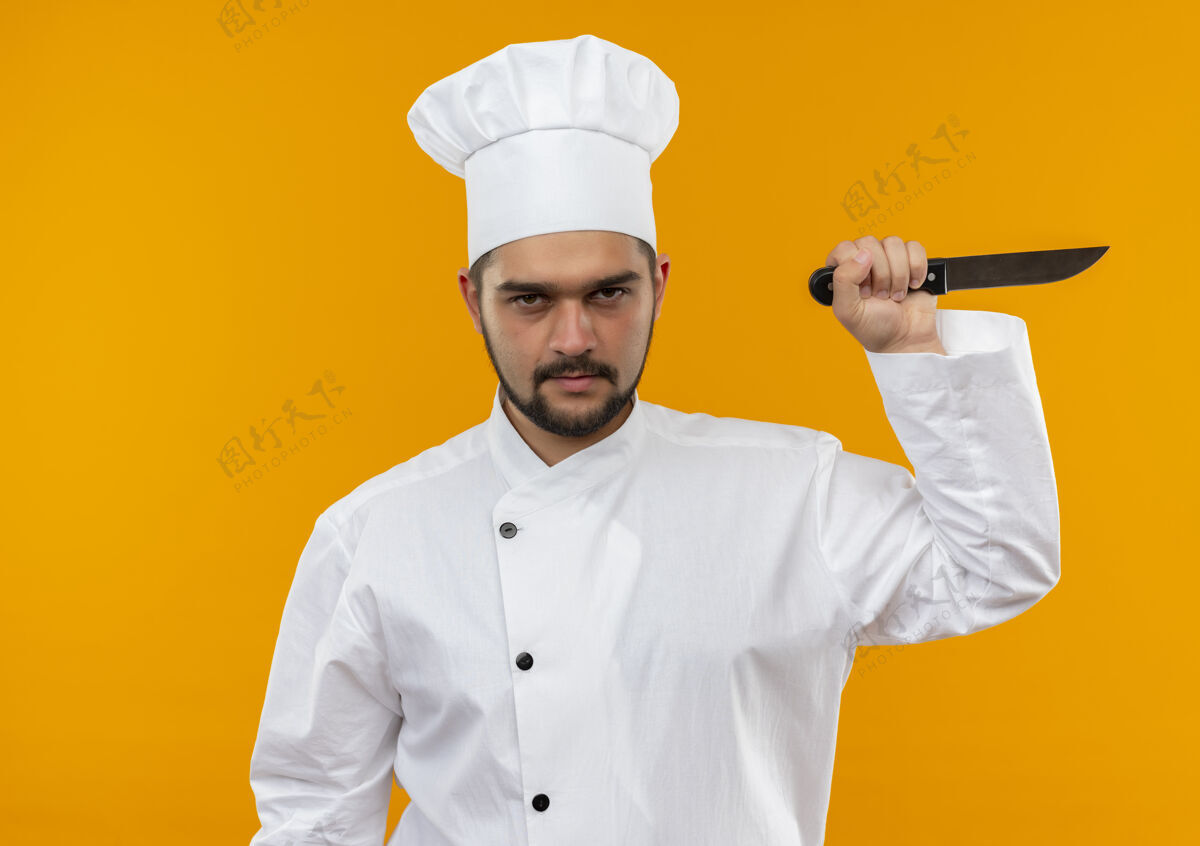 制服未出狱的年轻男厨师身着厨师制服 手持隔离在橙色空间的刀刀烹饪手持