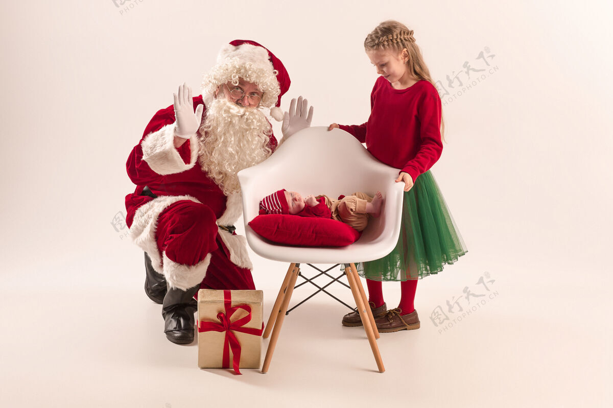 圣诞节可爱的新生小女婴和漂亮的妹妹穿着圣诞服装和圣诞老人的服装和帽子的男子圣诞画像帽子房子新生儿