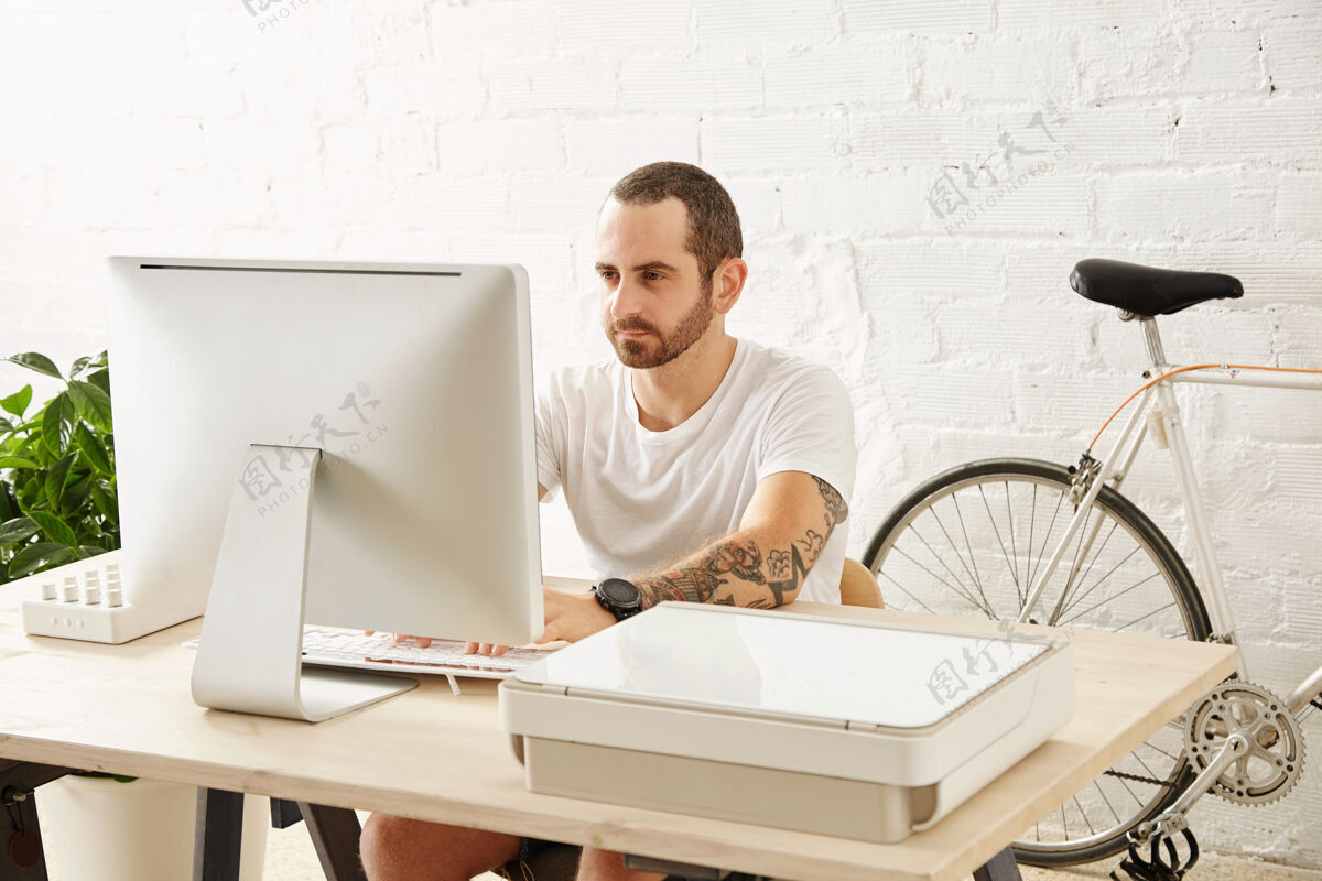 教育一个年轻的自由职业者穿着一件白色的t恤 在自行车旁的家里用电脑工作 正在看展览室内工作办公室