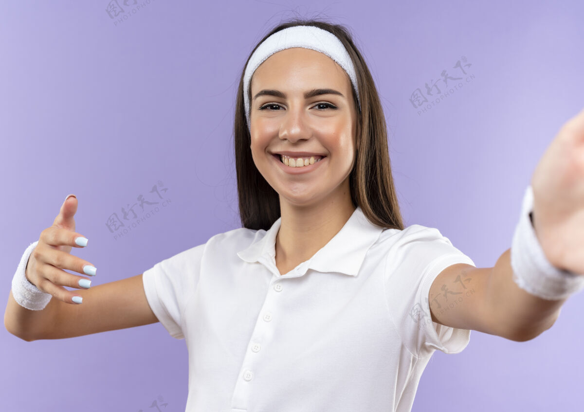 紫色微笑美丽的运动女孩戴着头带和腕带 举起的手孤立在紫色的空间抬高漂亮佩戴