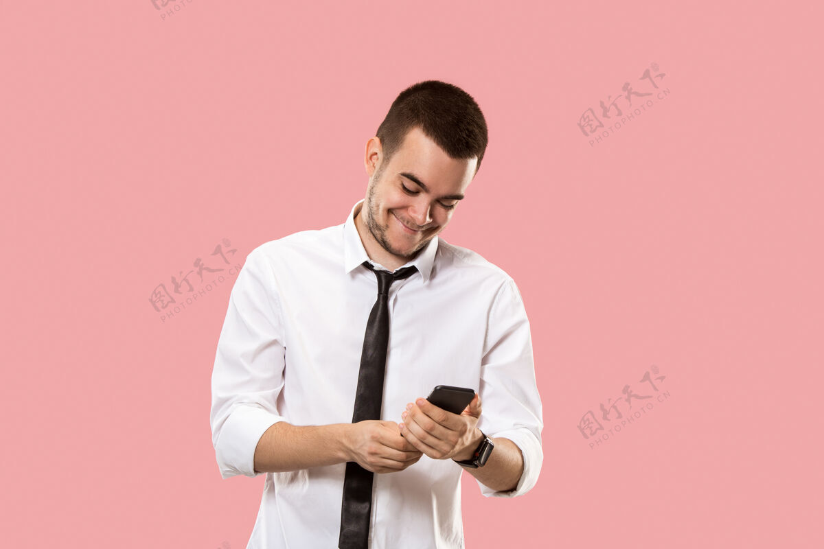 男性英俊的商人拿着手机年轻的商人孤零零地站在粉红色的墙上美丽的男性半身像工人老板短信