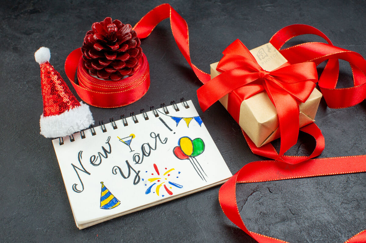 顶部顶视图的礼物针叶树锥与红丝带和笔记本与新年写作和圣诞老人帽子美丽的礼物在黑暗的背景笔记本柜台针叶树锥