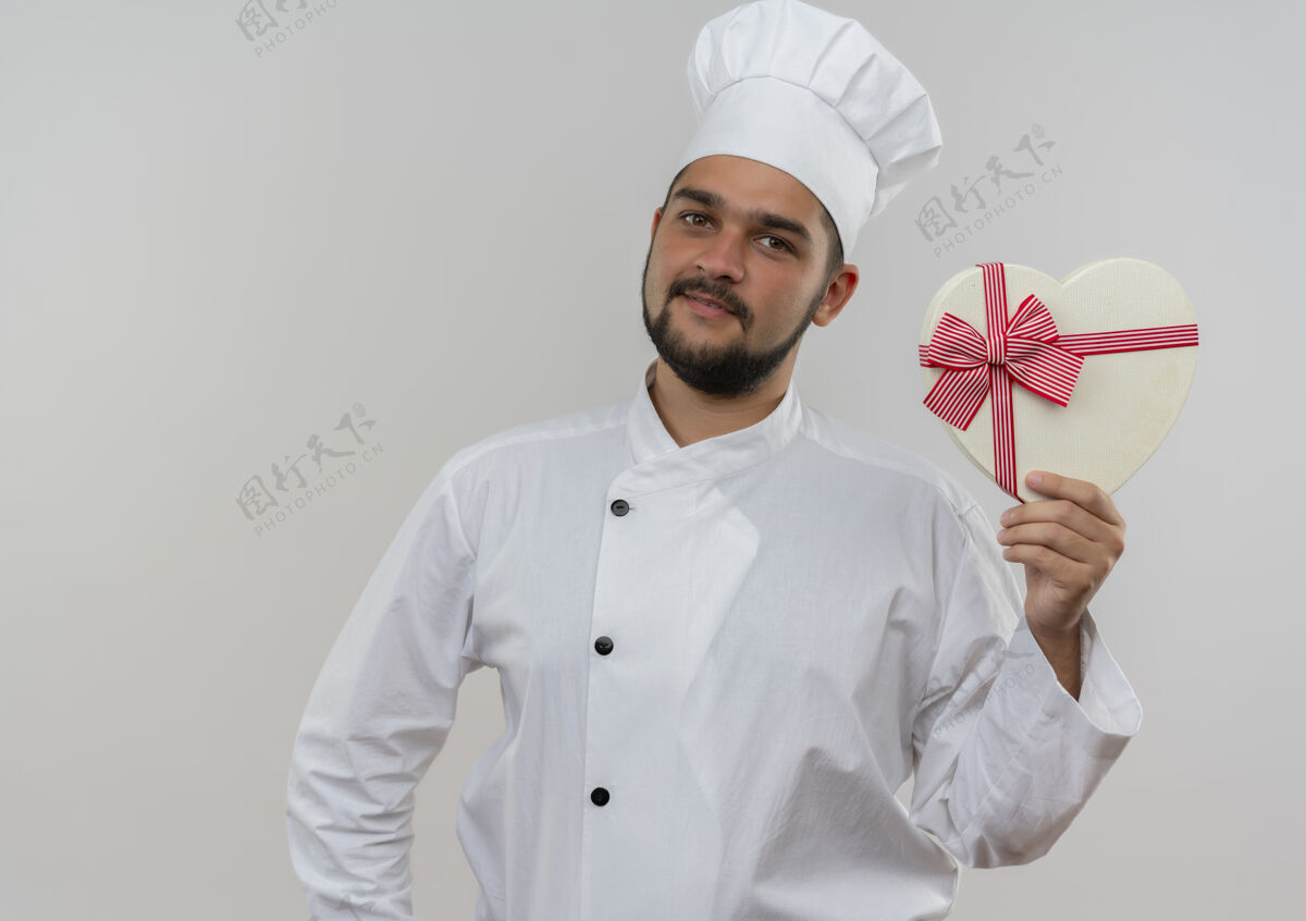 持有高兴的年轻男厨师身着厨师制服手持心形礼盒隔离在白色空间礼品厨师高兴