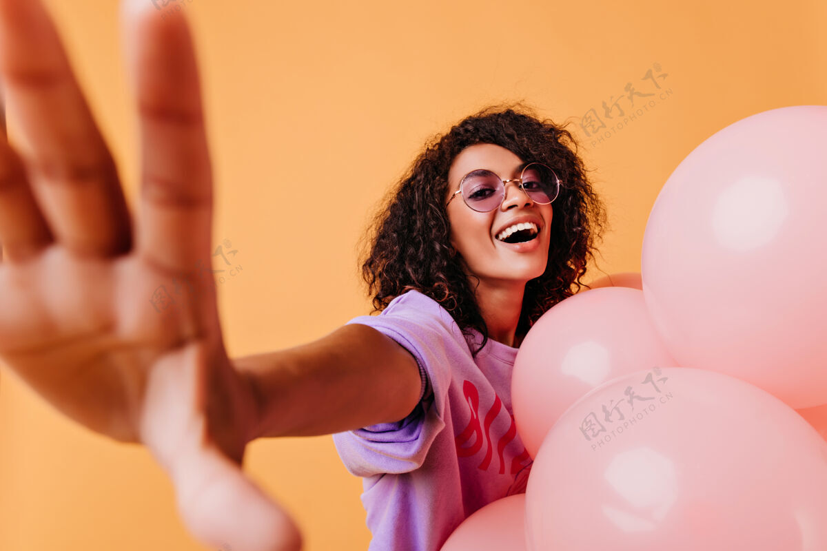 惊喜戴着时髦眼镜的漂亮生日女孩在自拍戴着可爱的粉色气球的非洲女人在黄色上大笑女人黑色欢快
