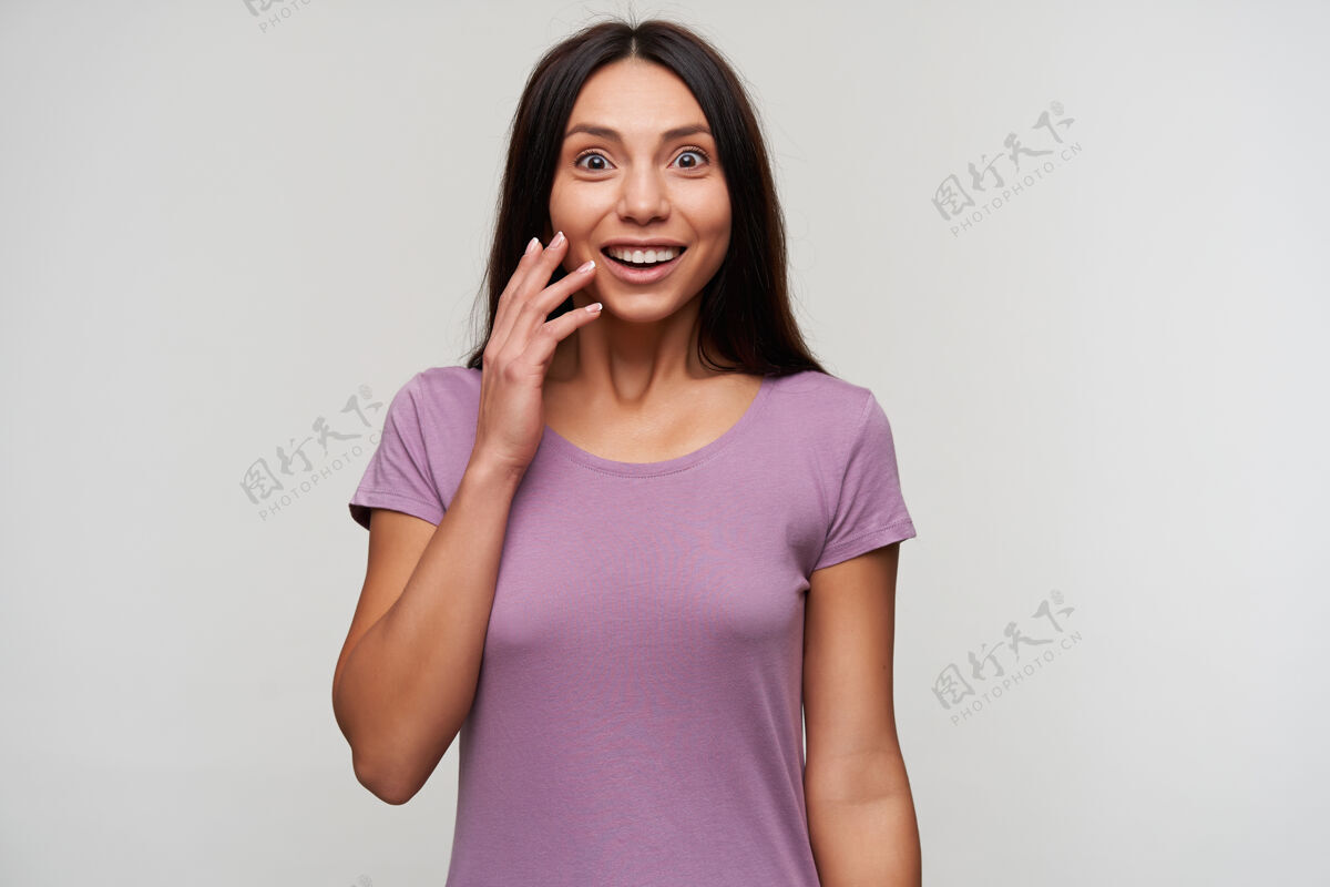 紫色睁眼的年轻漂亮黑发女人 随意化妆 手举在脸上 一边惊讶地看着 穿着紫色t恤 一边摆着白色的姿势休闲深色积极