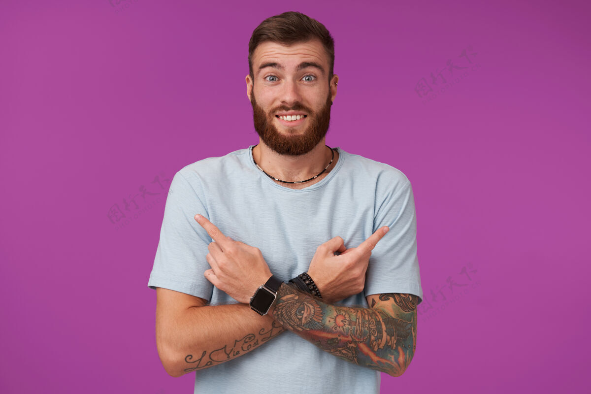 短裤快乐的年轻人 留着胡子 穿着蓝色t恤 双手交叉放在胸前 用食指在不同的侧面展示 扬起眉毛 微笑着紫色男人休闲手表