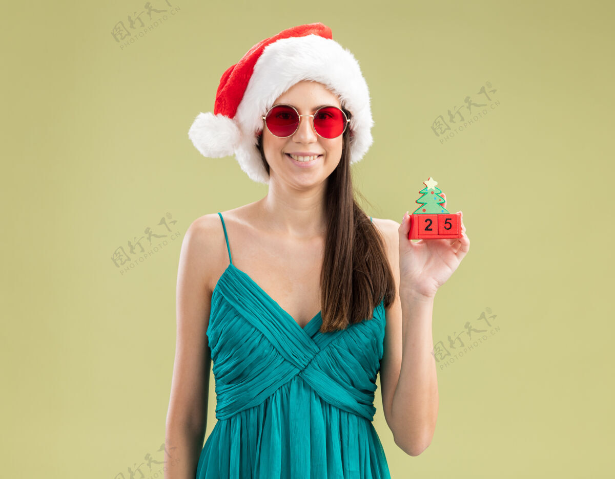 女孩戴着太阳眼镜 头戴圣诞帽 手拿圣诞树饰物 面带微笑的白人女孩空间圣诞圣诞快乐