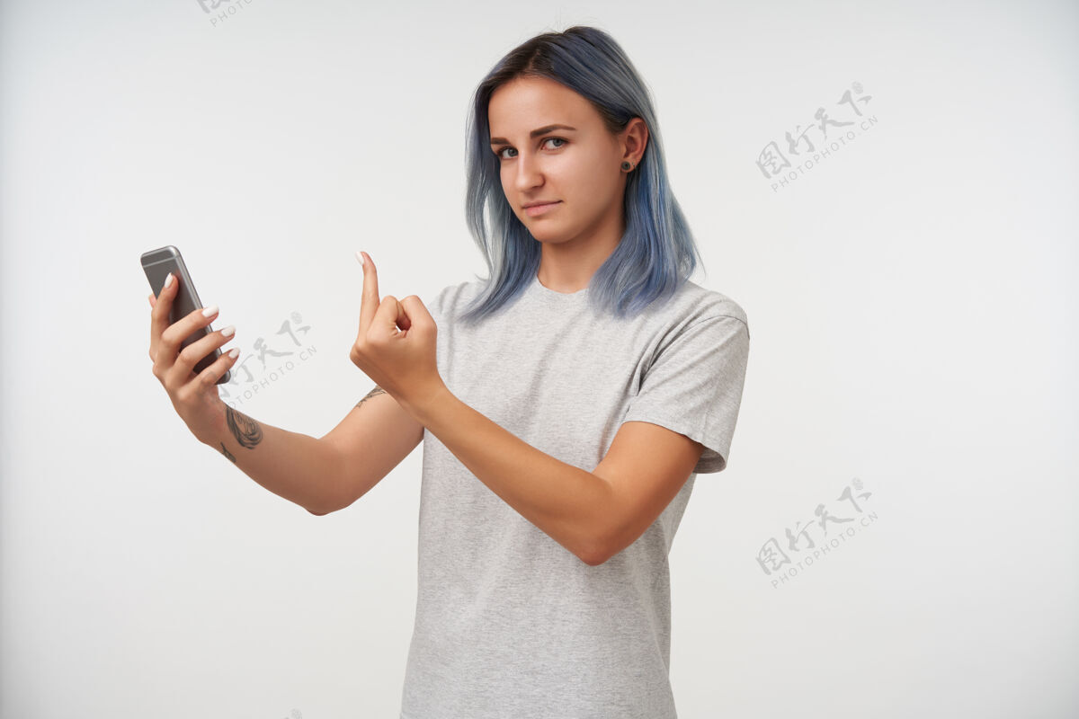 蓝色年轻的纹身女性的肖像 蓝色短发 用中指举起手 同时进行视频通话 站在白色的年轻女士自然