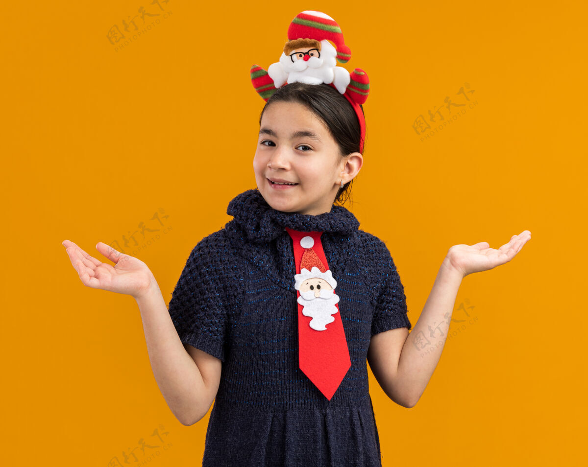 边缘小女孩穿着针织连衣裙 头上系着一条红色领带 头上戴着一个有趣的圣诞戒指 脸上洋溢着快乐的笑容 双臂向两边张开连衣裙圣诞快乐编织
