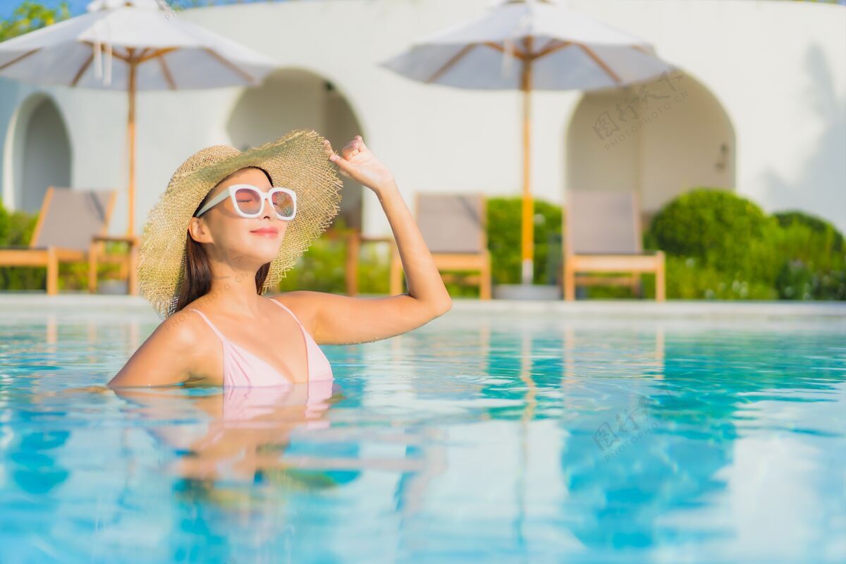 阳光肖像美丽的亚洲年轻女子放松休闲围绕室外游泳池与海比基尼无限度假村