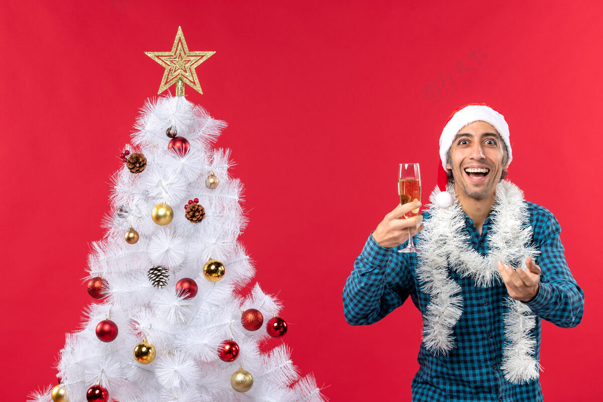 帽子滑稽的年轻人戴着圣诞老人的帽子 穿着蓝色的衬衫 手里拿着一杯酒庆典圣诞老人杯子