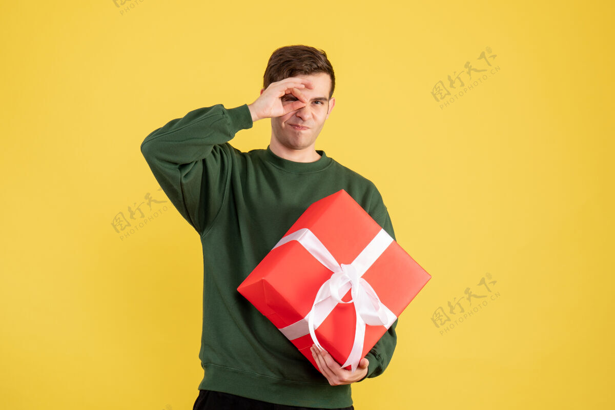 礼品正面图：穿着绿色毛衣的年轻人拿着黄色的圣诞礼物足球国旗绿色