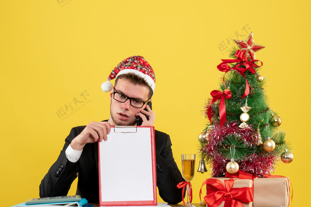 服装前视图：男员工在小圣诞树旁打电话 呈现淡黄色电话树礼物