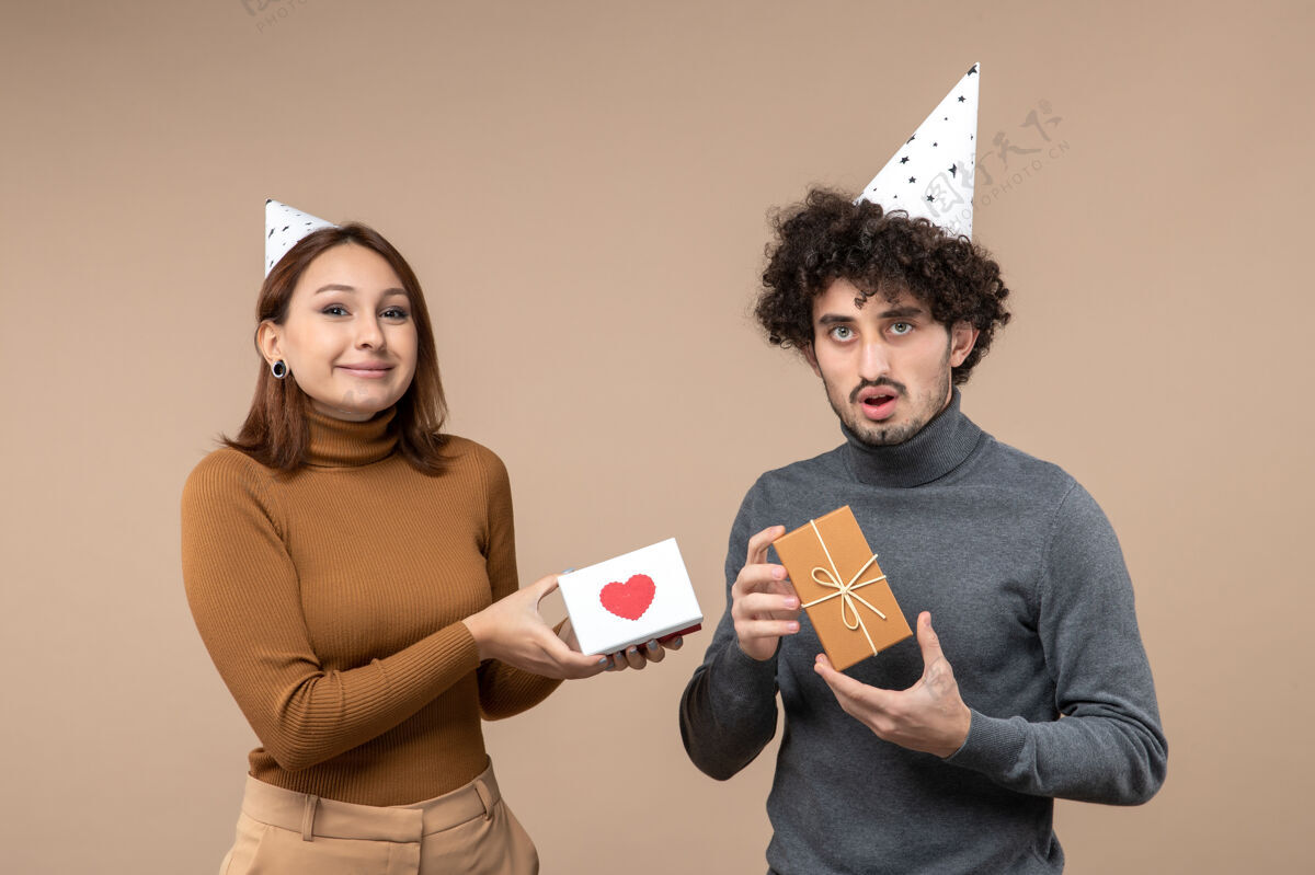 情侣新年拍摄与情感搞笑年轻夫妇戴新年帽女孩的心和男孩的礼物灰色礼物漂亮黑发