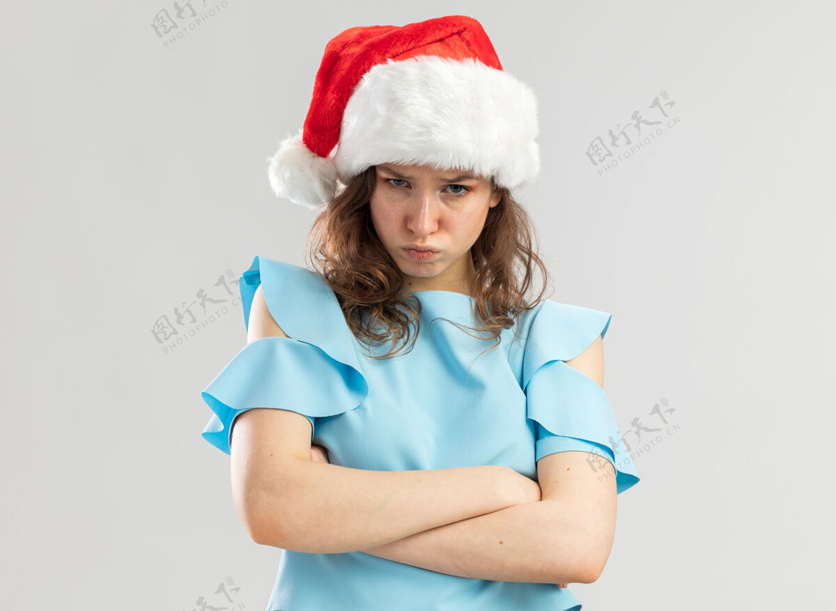 年轻一个穿着蓝色上衣 戴着圣诞帽 眉头紧锁 双臂交叉的愤愤不平的年轻女人站着新快乐