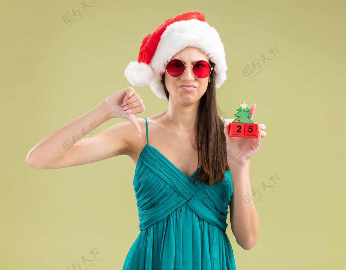 年戴着太阳眼镜 戴着圣诞帽 拿着圣诞树饰物 竖起大拇指的年轻白人女孩未发行持有装饰
