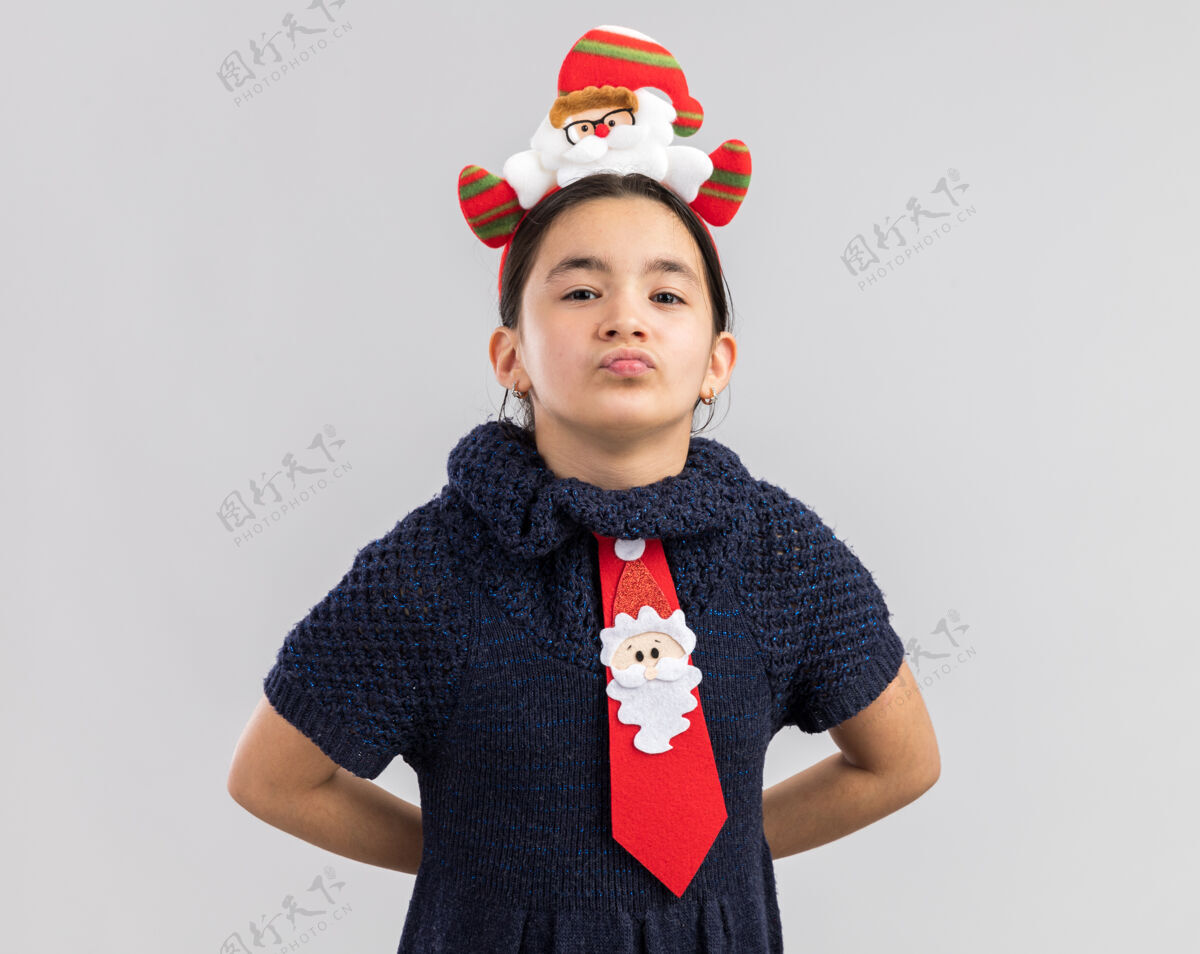 小小女孩穿着针织连衣裙 头上系着一条红色领带 头上戴着滑稽的圣诞戒指 脸上带着微笑领带新新年