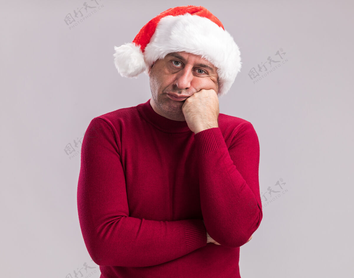 圣诞老人中年男子戴着圣诞老人的帽子 站在白色的背景下 看着镜头 又累又无聊中间圣诞快乐年龄