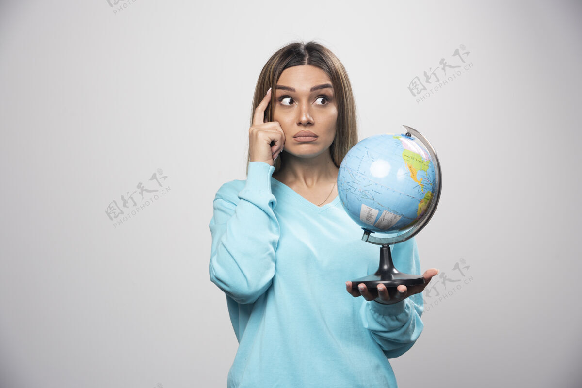 地理穿着蓝色运动衫的金发女孩手里拿着一个地球仪 仔细地思考 试图记住女性女性学习
