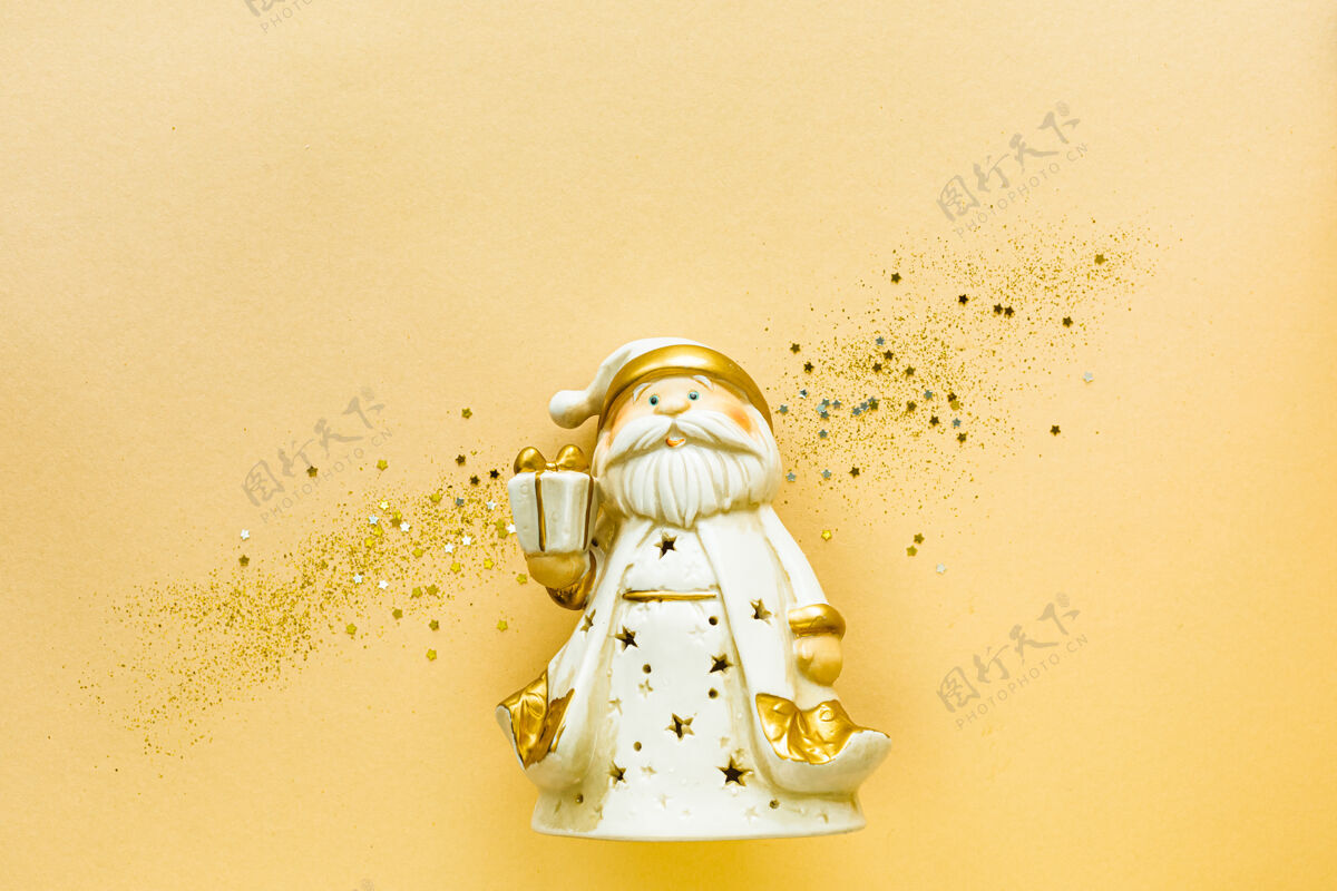 新的玩具圣诞老人用一个金色的礼品盒上的黄色背景假日概念 平放 俯视 复制空间花最小蜡烛