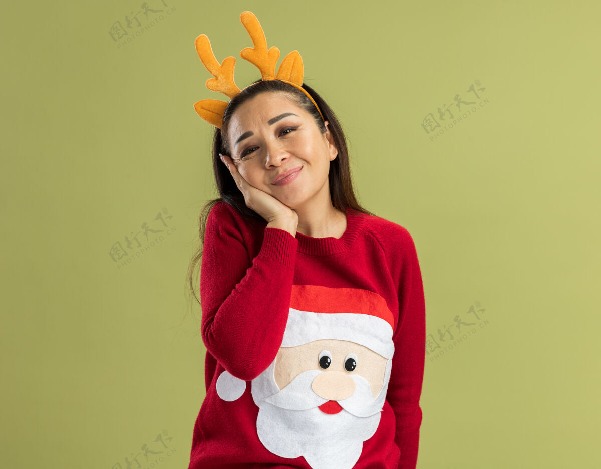 圣诞穿着红色圣诞毛衣的年轻女子 戴着滑稽的鹿角边 面带微笑 快乐而积极角脸毛衣