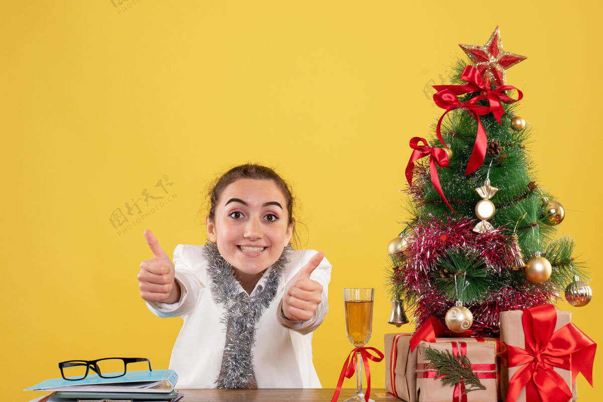 背景正面图：女医生围坐在黄色背景上的圣诞礼物和圣诞树旁健康前面女医生