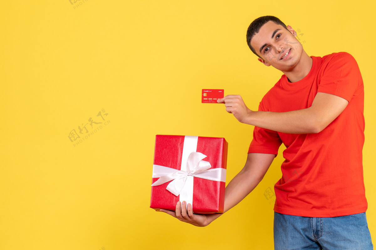 礼物黄墙上拿着礼物和银行卡的年轻人的正视图十二月年轻男性漂亮