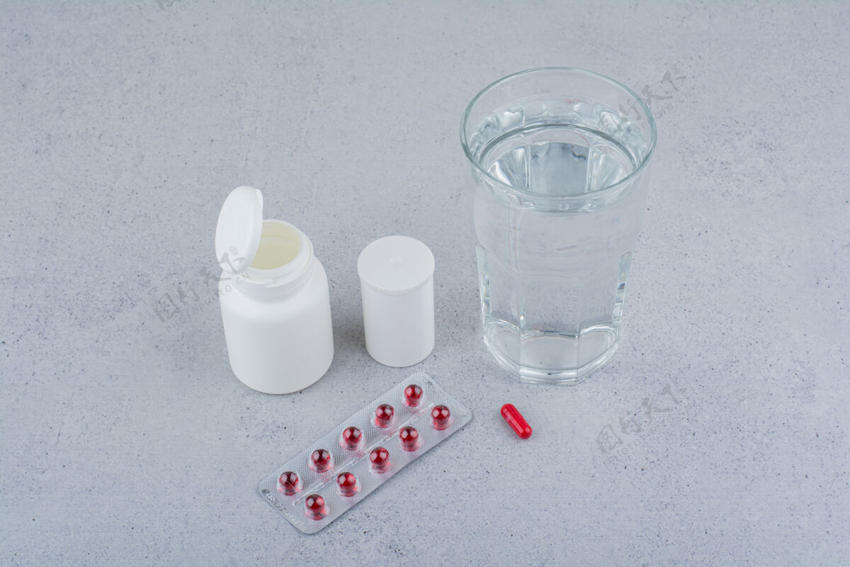 片剂红色的药丸 容器和一杯水在大理石表面补充剂止痛药抗生素