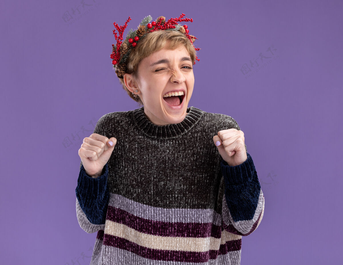 圣诞节快乐的年轻漂亮女孩戴着圣诞花环眨眼做是的手势孤立在紫色的墙上戴年轻花环
