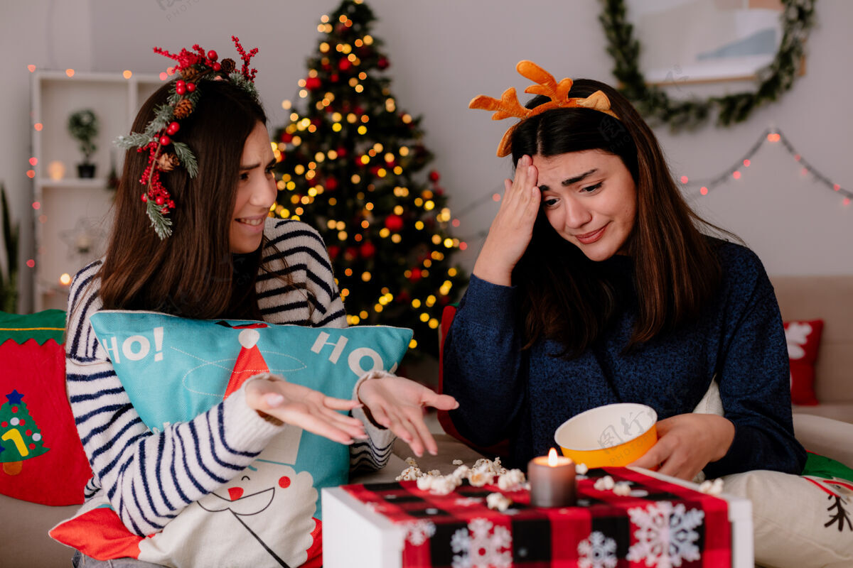 年轻带着驯鹿头带的焦急漂亮的小女孩看着扔在扶手椅上的爆米花和朋友在家过圣诞节圣诞快乐掉下来了看起来
