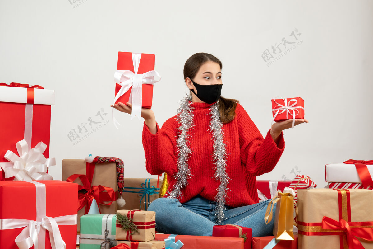 成人戴着黑色面具的年轻圣诞女孩双手捧着礼物围坐在白色的礼物上两者礼物年轻