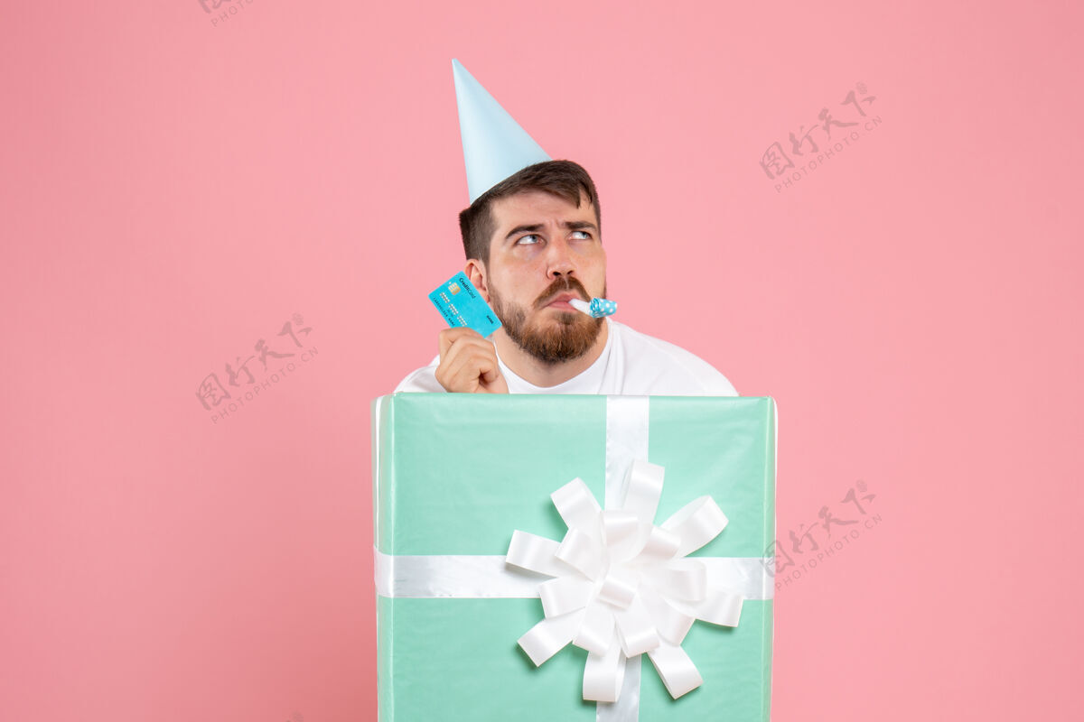 男性粉红色墙上拿着银行卡的盒子里的年轻人的正视图里面圣诞节情感