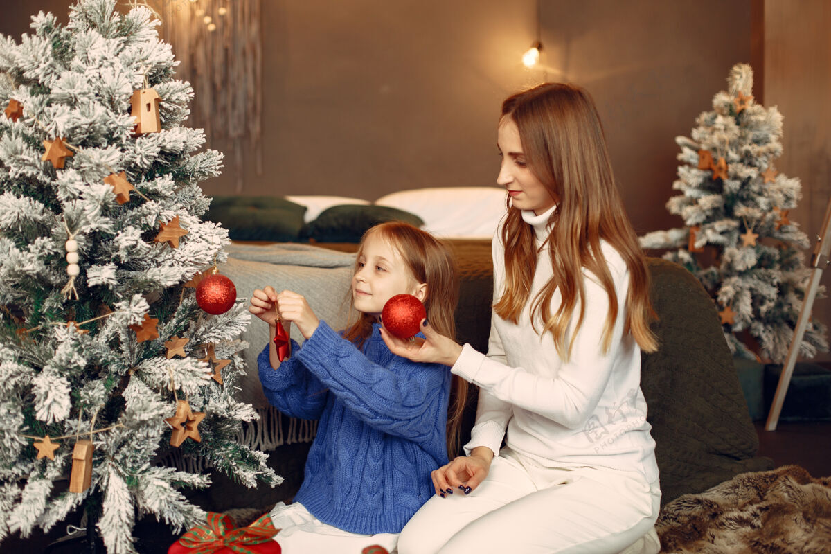 给人们在为圣诞节做准备母亲在和女儿玩耍一家人在节日的房间里休息孩子穿着蓝色毛衣人女孩节日