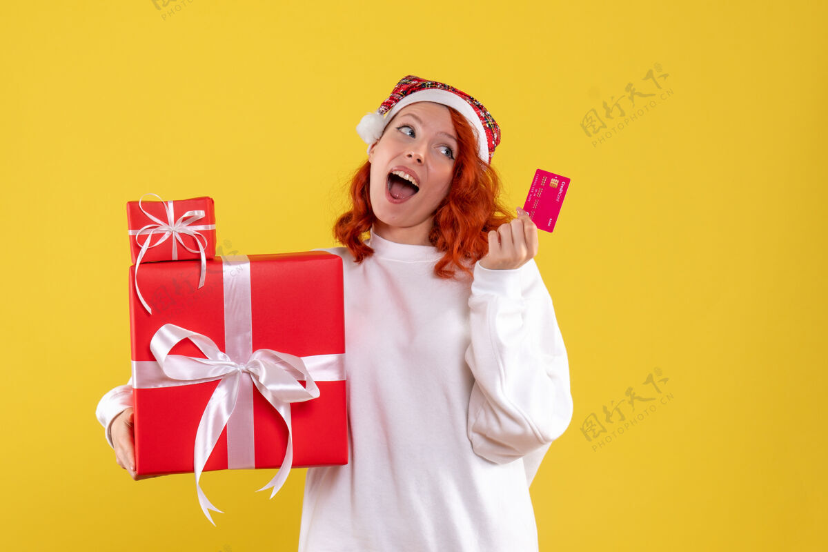 女人黄墙上年轻女子拿着圣诞礼物和银行卡的正面图微笑情感年轻的女人