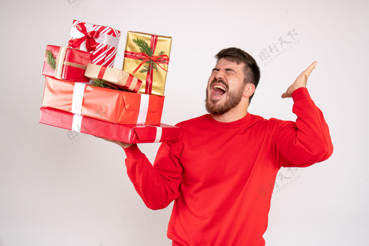 快乐一个穿着红衫的年轻人拿着圣诞礼物站在白色的墙上人微笑年轻男性