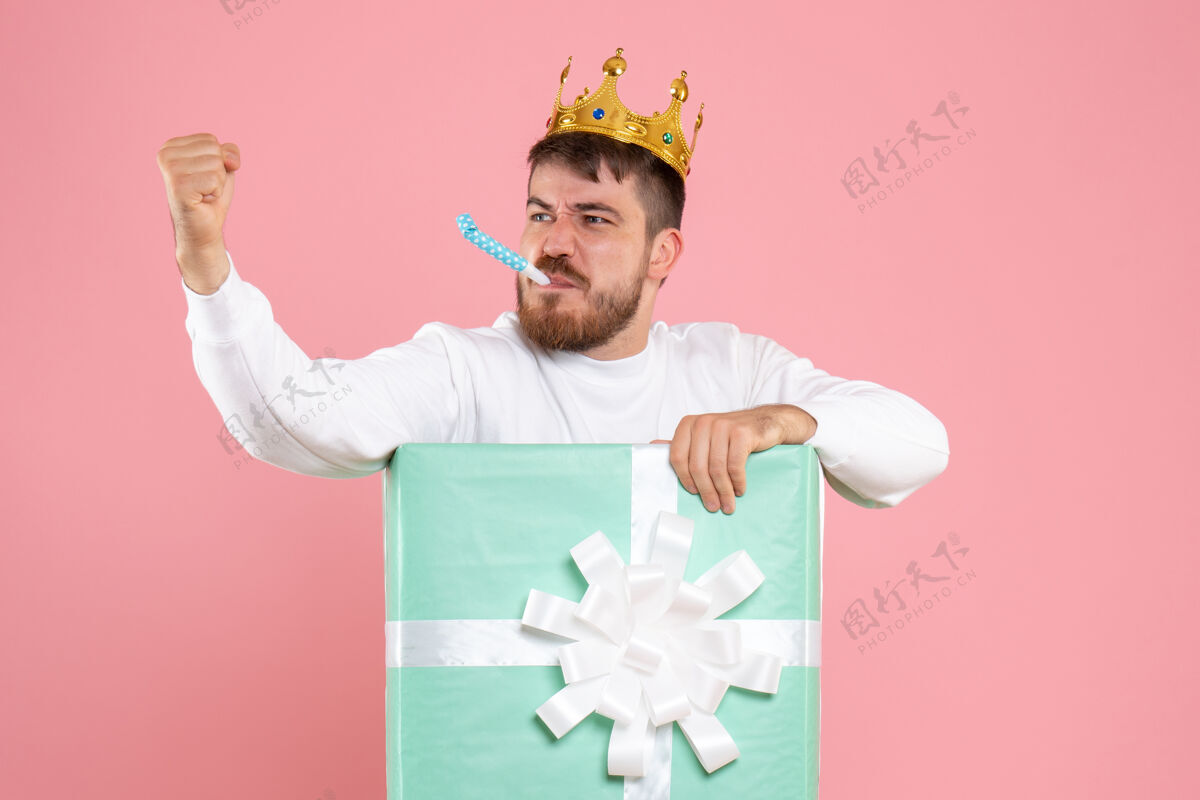 男性礼物盒内年轻人的正面图 粉红色墙上有人戴着王冠威胁着他圣诞节情感内部