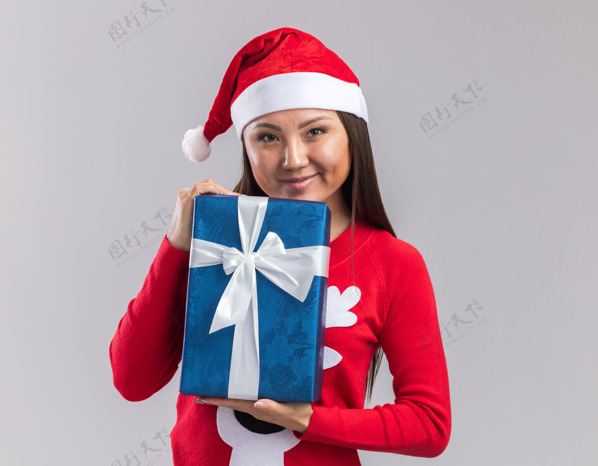 拿着高兴的年轻亚洲女孩戴着圣诞帽和毛衣拿着礼品盒隔离在白色背景上礼物帽子毛衣