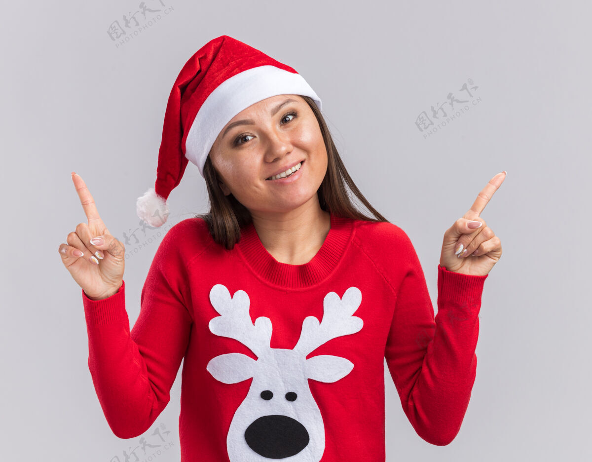 倾斜微笑歪着头的年轻亚洲女孩戴着圣诞帽 毛衣点在白色背景上孤立起来毛衣年轻头