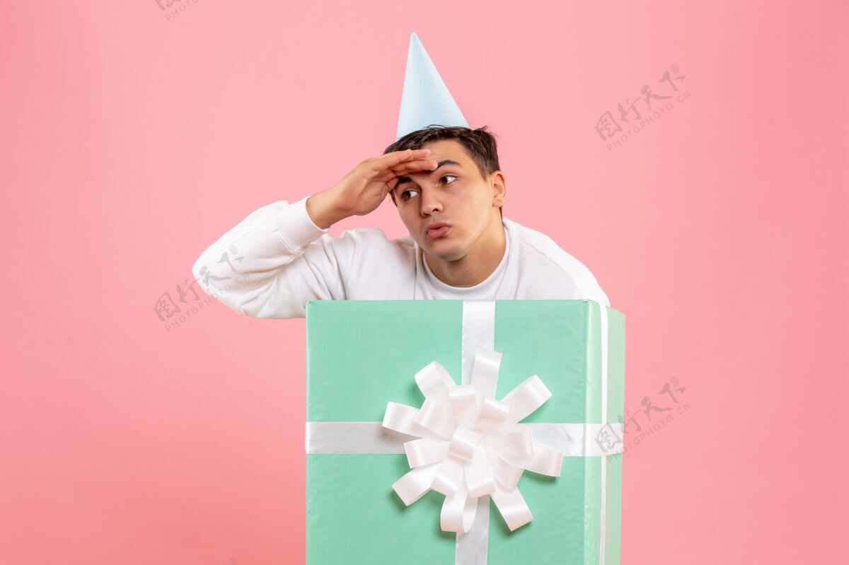 盒子隐藏在粉红色墙上的礼物里面的年轻人的正面视图举行年轻男性前面