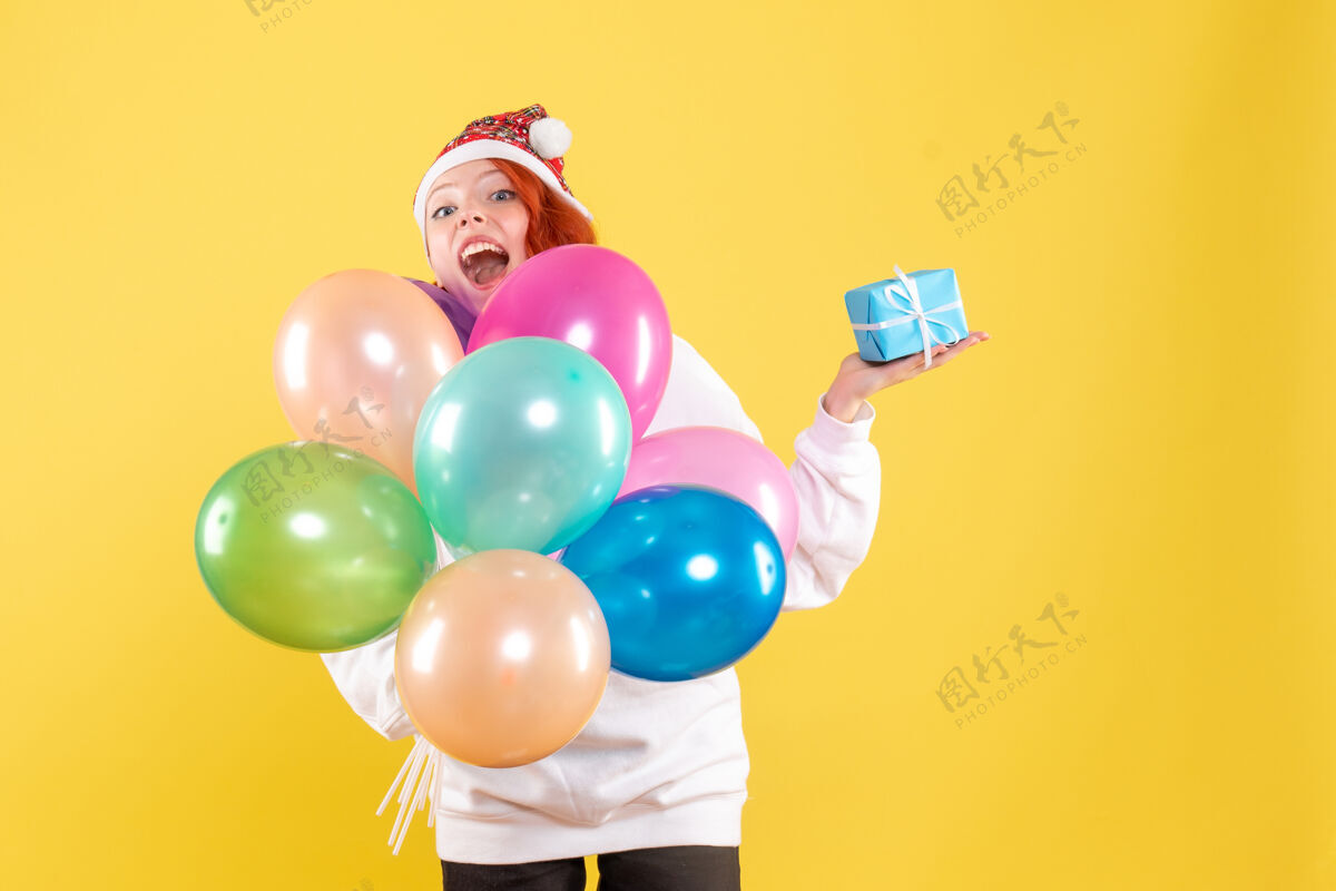 圣诞节黄色墙上拿着小礼物和彩色气球的年轻女子的正视图前面乐趣年轻