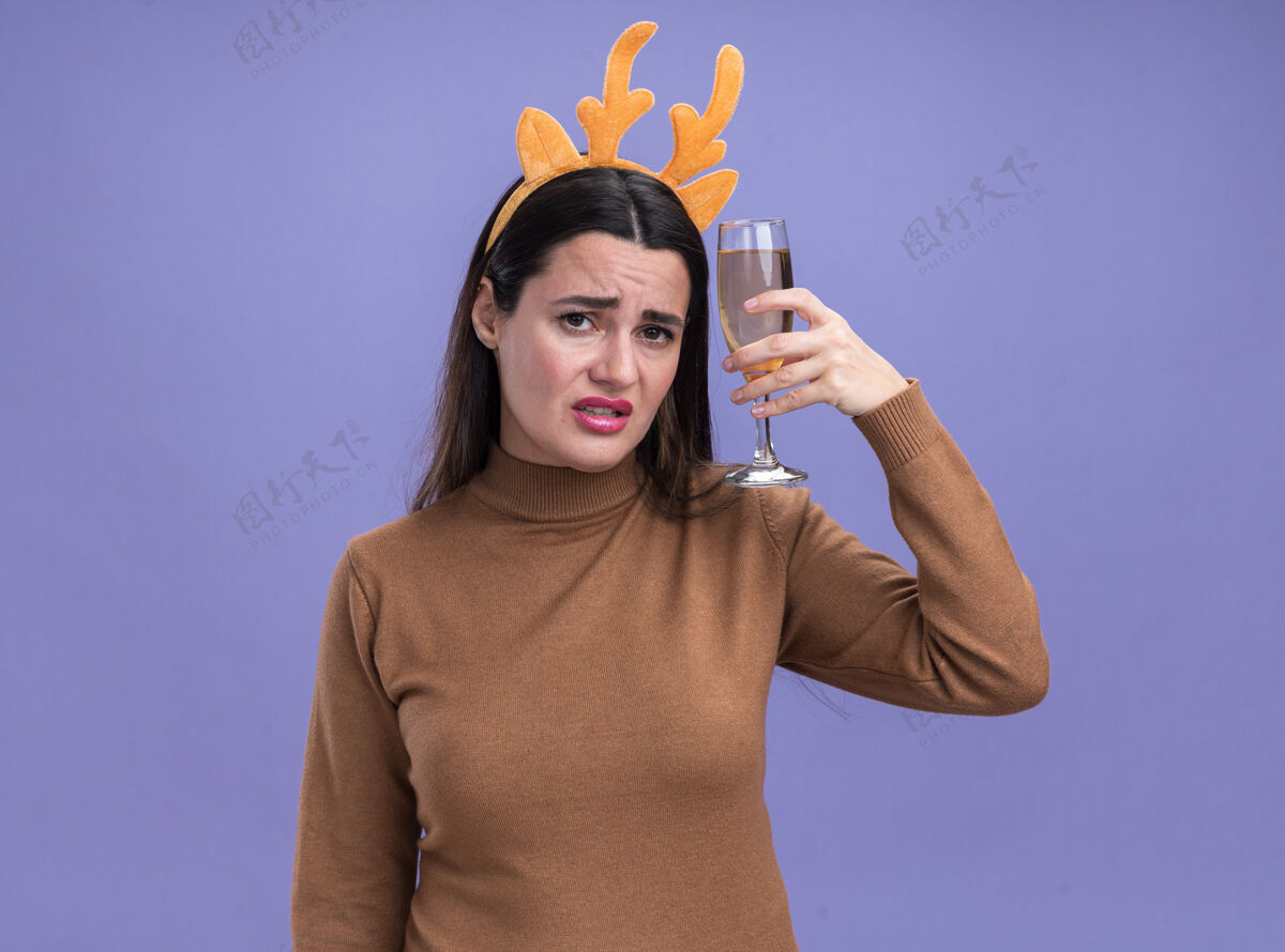 圣诞节未出嫁的年轻漂亮女孩 穿着棕色毛衣 戴着圣诞发箍 肩上扛着一杯香槟酒 背景是蓝色的箍肩头发