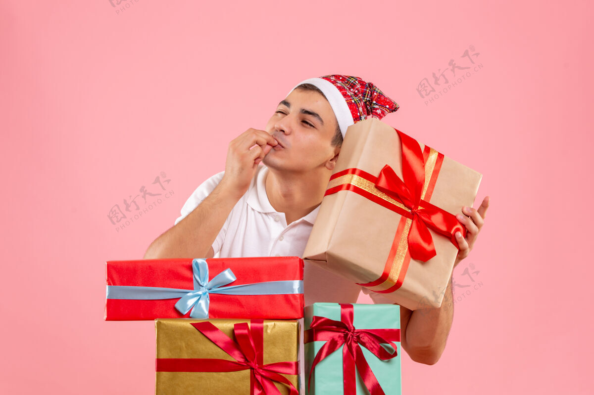 年轻男性年轻人围着粉色墙上不同圣诞礼物的前视图礼物人类人