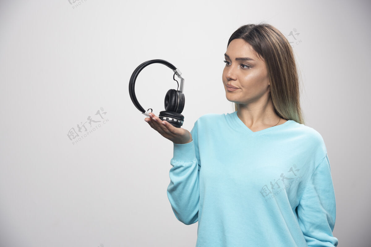 积极穿着蓝色运动衫的金发女孩拿着耳机 准备戴上耳机听音乐年轻听耳机