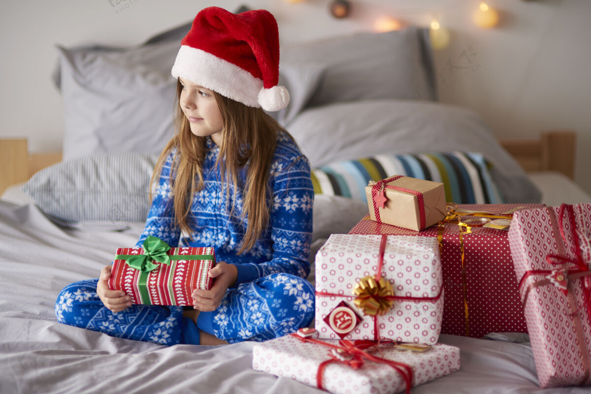 孩子床上可爱的女孩拿着圣诞礼物小牙牙牙学语的微笑圣诞帽